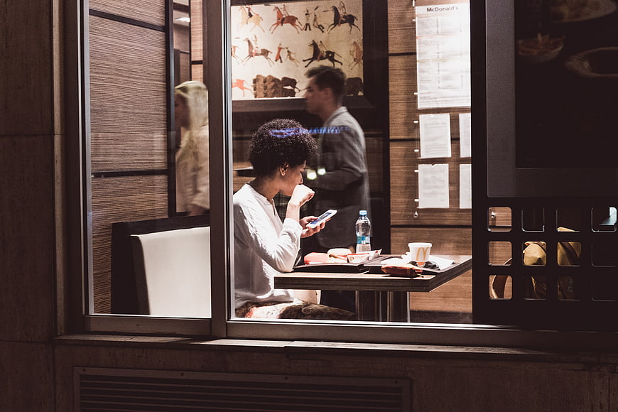 Woman using smartphone while eating at McDonald's window