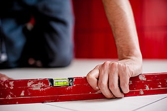 Carpenter using red spirit level on white floor tiles