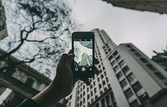 Hand holding smartphone taking photo of city skyscraper