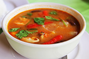 Close-up of spicy red Thai curry soup with seafood and herbs