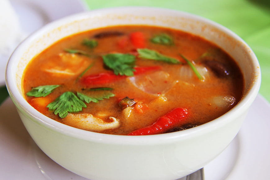 Close-up of spicy red Thai curry soup with seafood and herbs