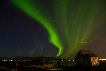 Aurora Borealis over a wooden cabin and stargazer at night