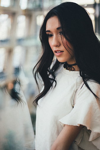 Young woman with dark hair looking away in white top