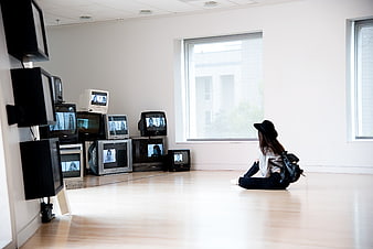 Woman sitting on floor watching multiple vintage televisions in white room