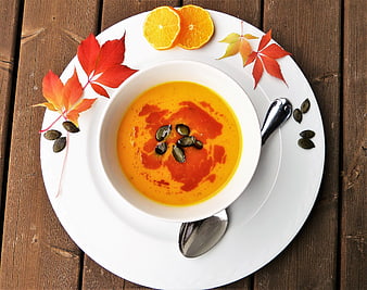 Overhead view of creamy pumpkin soup with seeds and autumn leaves