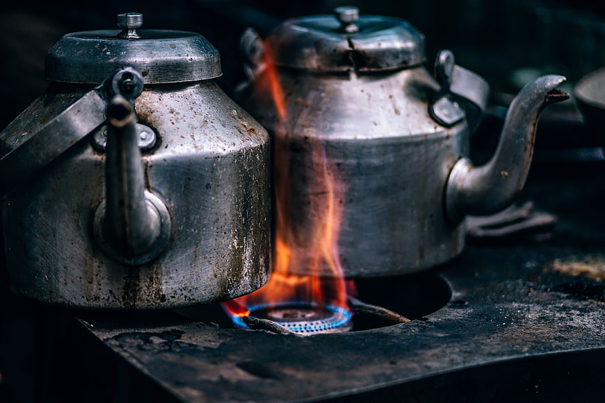 Two vintage metal kettles on a gas stove with flame