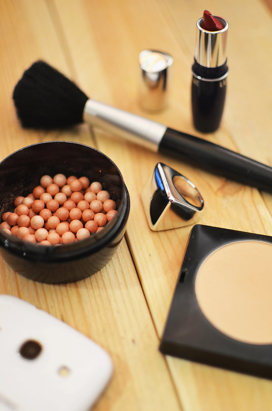 Assorted Makeup Products and Brush on Wooden Table