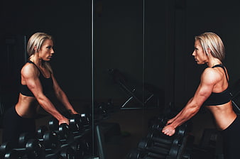 Athletic Blonde Woman Selecting Dumbbells in Dark Gym