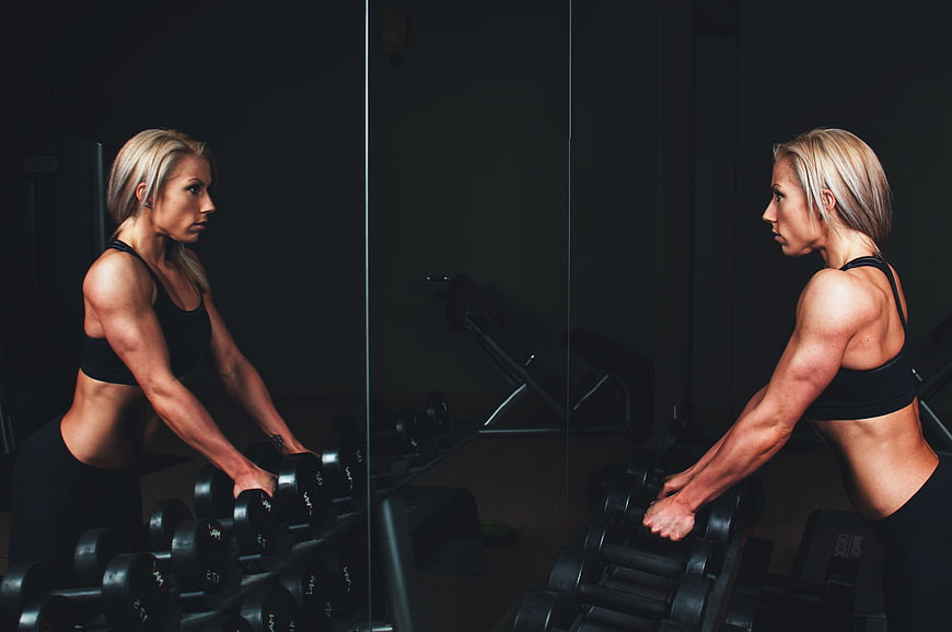 Athletic Blonde Woman Selecting Dumbbells in Dark Gym