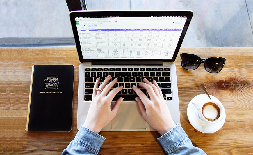 Top view of hands typing on laptop with coffee and notebook
