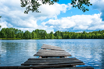 Weathered wooden pier extending into a calm blue lake with forest background