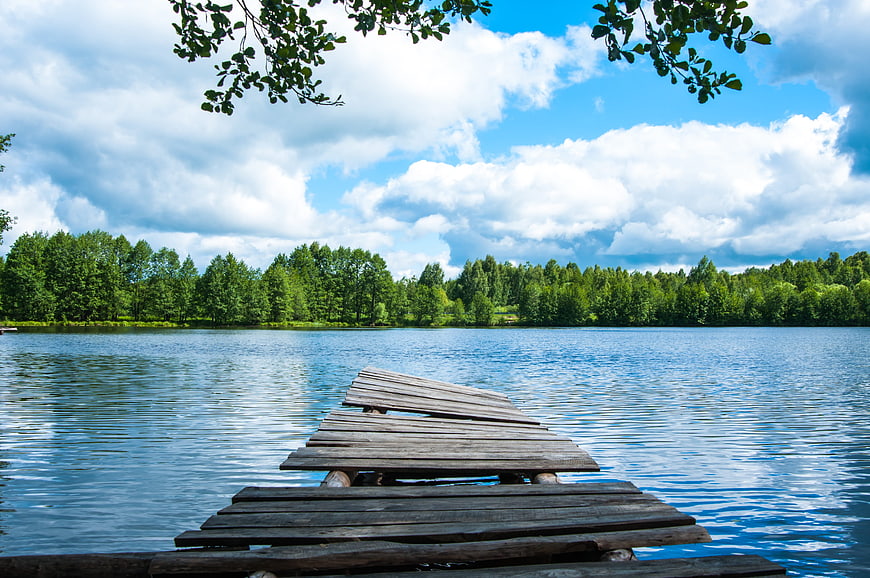 Weathered wooden pier extending into a calm blue lake with forest background