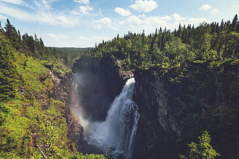 Majestic waterfall cascading into a misty forest canyon