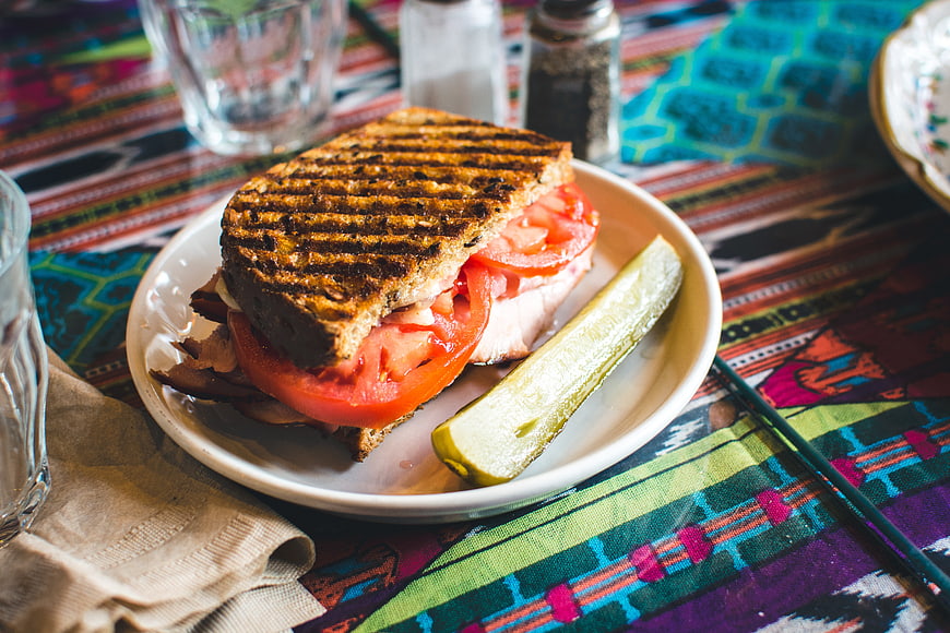 Grilled sandwich with tomato and pickle on colorful tablecloth
