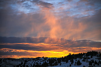 Dramatic Winter Sunset Over Snowy Pine Hills