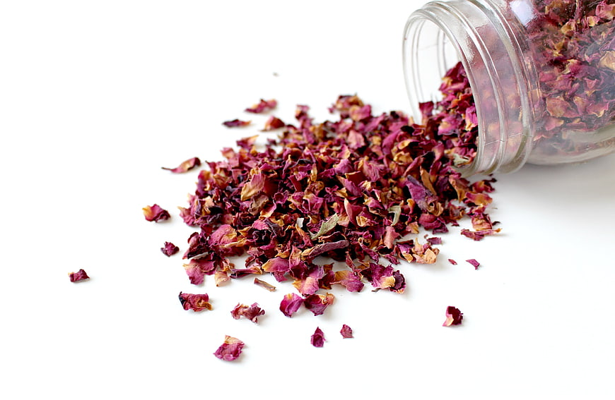 Dried Rose Petals Spilling from Glass Jar on White Background