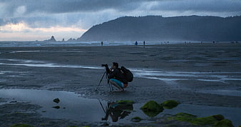 Photographer capturing moody coastal landscape at low tide