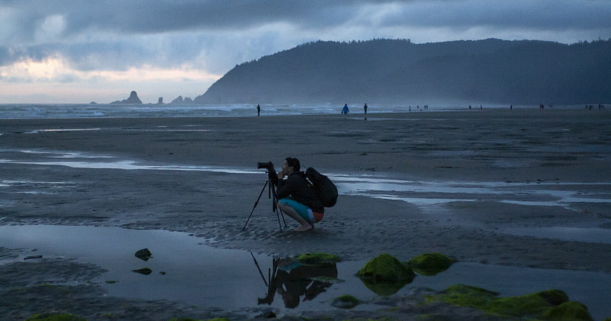 Photographer capturing moody coastal landscape at low tide