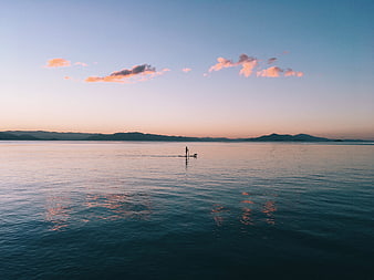 Silhouette of Stand Up Paddleboarder on Calm Ocean at Sunset