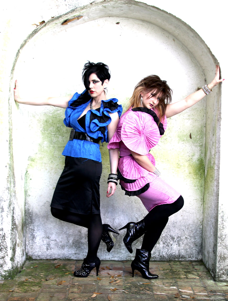 Two women in colorful retro fashion posing in an archway