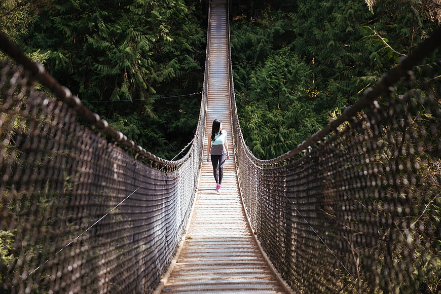 Woman Walking on Wooden Suspension Bridge in Forest