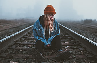 Sad woman sitting on foggy train tracks in winter