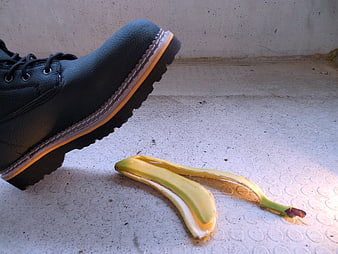 Black boot about to step on banana peel on concrete floor