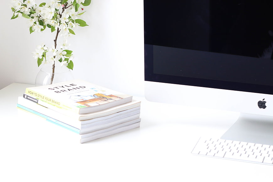 Minimalist white office desk with books, computer, and flowers