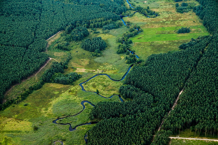 Aerial view of winding river through green forest and meadow