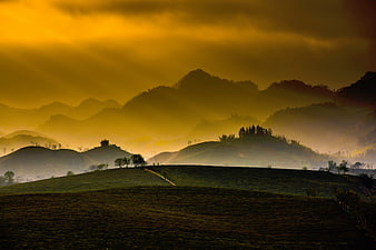 Golden misty mountain landscape with rolling green hills