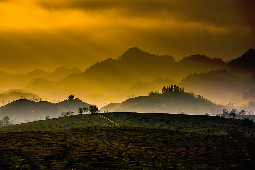 Golden misty mountain landscape with rolling green hills