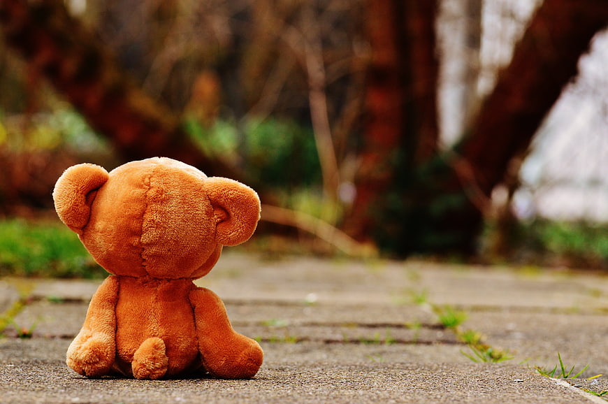 Lonely brown teddy bear sitting on a concrete path in a park