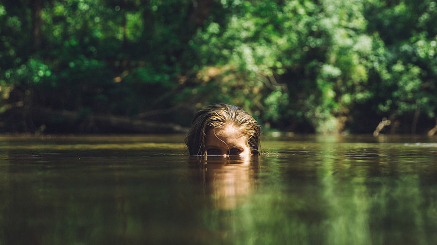 Woman's Eyes Peeking Over Water Surface in Forest