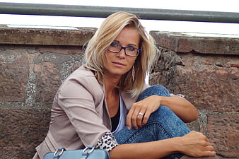 Blonde woman with glasses sitting against a rustic stone wall