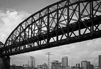 Black and white steel truss bridge over city skyline