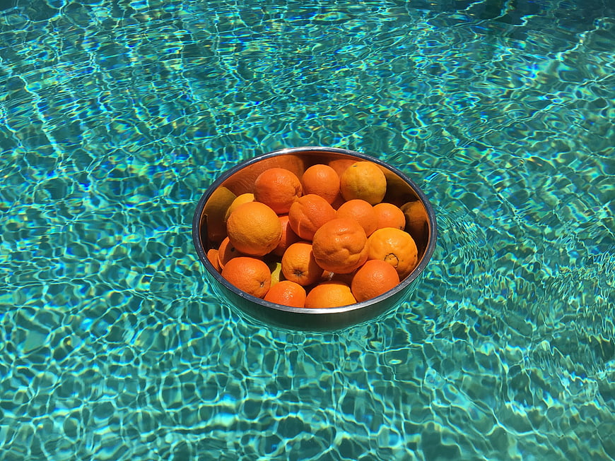 Bowl of Oranges Floating in Clear Blue Pool Water