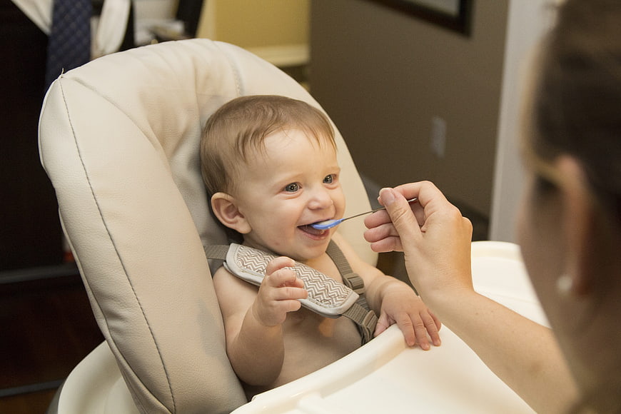 Happy baby eating solid food in high chair