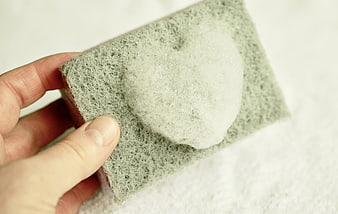 Hand holding sponge with heart-shaped foam for cleaning