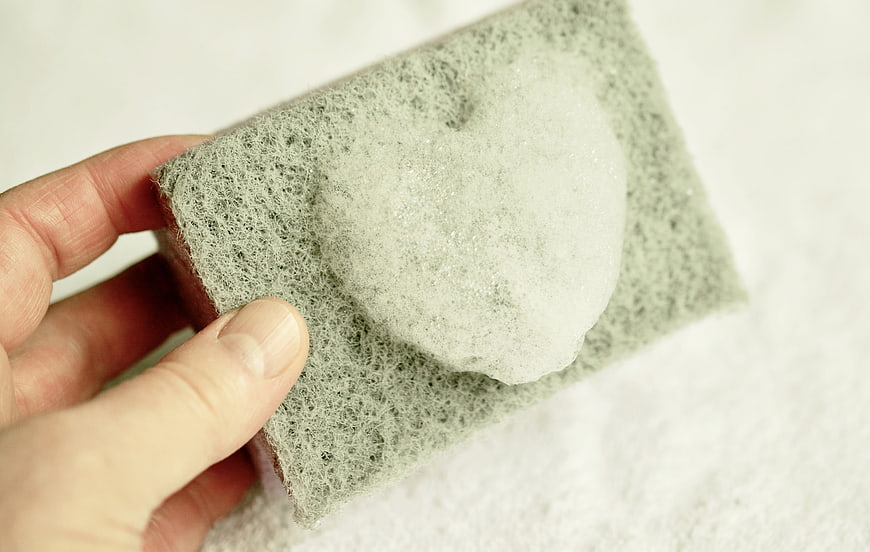 Hand holding sponge with heart-shaped foam for cleaning