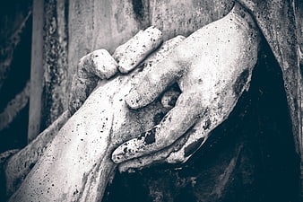 Close-up of weathered stone hands on a tombstone statue