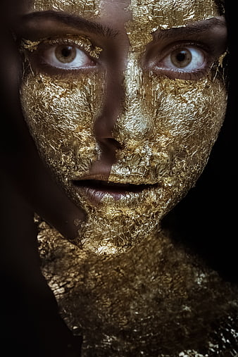 Close-up portrait of a woman's face covered in textured gold leaf