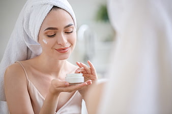 Woman applying face cream in bathroom mirror