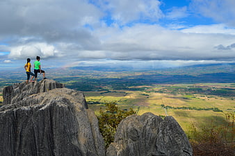 Two women hiking on rocky mountain peak overlooking vast valley
