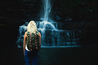 Woman with Backpack Standing Before Dark Waterfall