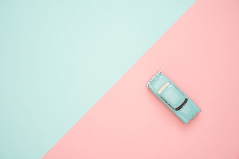 Top view of mint green toy car on pastel pink and blue background