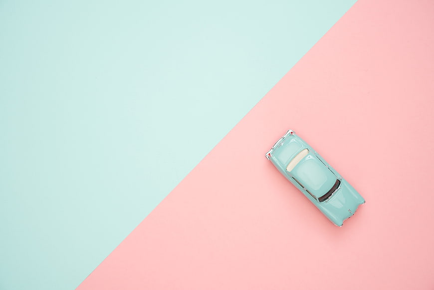 Top view of mint green toy car on pastel pink and blue background