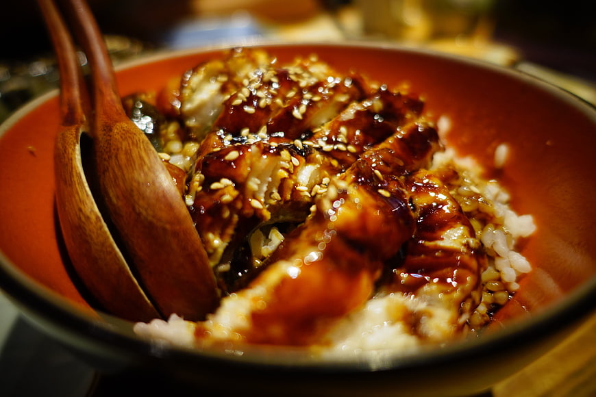 Glossy Japanese Eel Rice Bowl With Sesame Seeds And Wooden Spoons