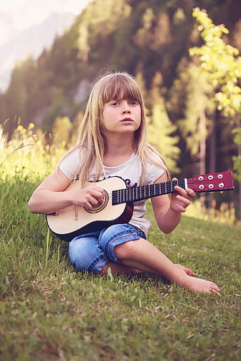 Young blonde girl playing acoustic guitar in a grassy field
