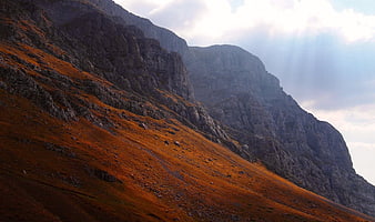 Dramatic Mountain Slope with Golden Hour Sunlight and Clouds