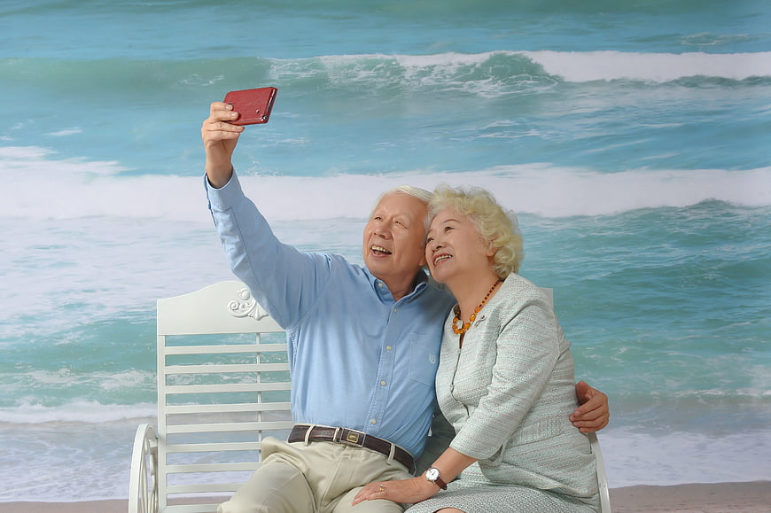 Senior Asian couple taking selfie on beach backdrop